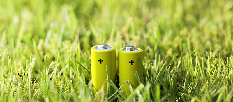 Two green batteries are standing on a patch of grass
